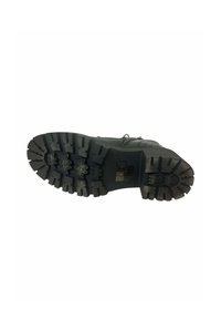 Suela de bota de goma negra con surcos profundos, que presenta patrones en zigzag y un logotipo rectangular enmarcado en un fondo negro.