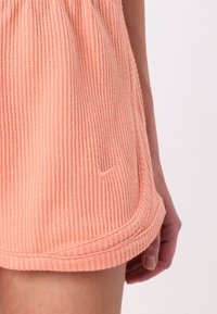 Peach ribbed shorts made of soft fabric, featuring a rounded hem and a small Nike logo on the lower side.