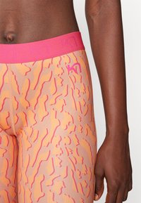 Høyt midje leggings i ferskenfarge med abstrakte oransje og rosa mønstre. Har en rosa elastisk livrem med logo-detaljer.