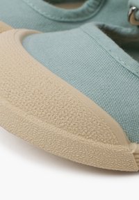 Zapatilla de lona azul claro con una suela de goma crema texturizada. Presenta una puntera redondeada y costuras visibles a lo largo de los bordes.