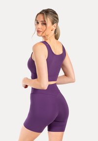 Paars sport crop top en hoge taille shorts van glad, rekbaar materiaal. Heeft brede bandjes en een naadloos ontwerp voor comfort.