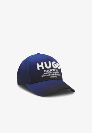 Blauwe honkbalpet met "HUGO" geborduurd in grote witte letters en extra kleinere witte tekst eronder op het voorpaneel.