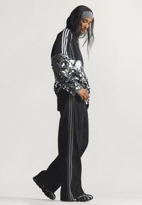 Μαύρο αθλητικό τοπ με μανίκια από παγιέτες, σε συνδυασμό με μαύρο παντελόνι φαρδύ στο πόδι με ρίγες στο πλάι. Συνδυασμένο με γκρι κορδέλα για τα μαλλιά και μοναδικά παπούτσια.