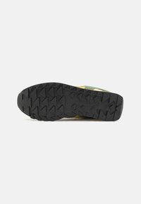 Black rubber sole with prominent treads, featuring multi-colored upper in green, yellow, and cream, designed for traction and stability.