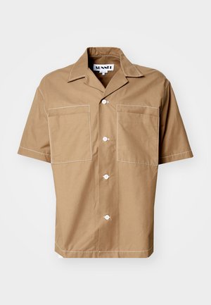 Lys beige skjorte med korte ærmer laget av bomull. Har spredd krage, to frontlommer og hvit søm langs sømmene.