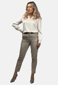 Biała bluzka z dekoltem w kształcie litery V i długimi rękawami, w zestawie z beżowymi, dopasowanymi spodniami i wzorzystymi szpilkami. Ma czarny pasek z srebrną klamrą.