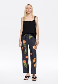 Black sleeveless top with thin straps, paired with dark pants featuring floral orange and green patterns. Flat sandals with textured straps.