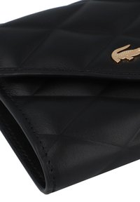 Portafoglio in pelle trapuntata nera con logo di coccodrillo in tono oro e dettagli di cucitura visibili. La texture liscia ne migliora il design complessivo.