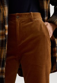 Bruine corduroy broek met een knoopsluiting, zijzakken en gestructureerde verticale strepen, gecombineerd met een geruite jas.