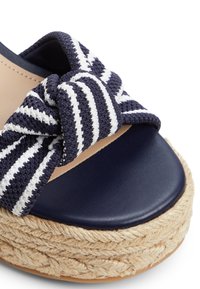 Sandale compensée à brides avec un dessus en tissu rayé bleu marine et blanc noué, une plateforme lisse bleu marine, et une semelle texturée en jute.