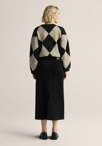 Svart och krämfärgad argyle-mönstrad tröja med ballongsärmar, kombinerad med en lång svart denimkjol och svarta skor; enfärgad texturerad bakgrund.