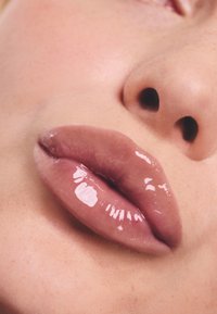 Błyszczący, cielisty kolor ust z gładką teksturą. Zbliżenie na pełne usta, podkreślające subtelny połysk i naturalne kontury ust.