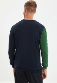 Pull en corps bleu marine, avec des manches vertes, des poignets côtelés et un col rond. Texture lisse sans motifs ni accents visibles.