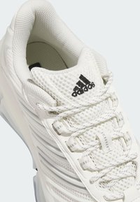 Chaussure de sport blanche Adidas avec tige en mesh, col rembourré, lacets réfléchissants et logo Adidas noir sur la languette.
