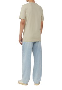 Beige katoenen t-shirt met een ronde hals, korte mouwen, gecombineerd met lichtblauwe, loszittende denim jeans en lichtgekleurde sneakers.