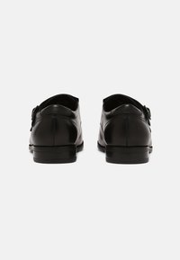Zapatos de cuero negro con un acabado suave, punta redondeada y un tacón bajo apilado. Presentan un detalle de hebilla en el lateral.