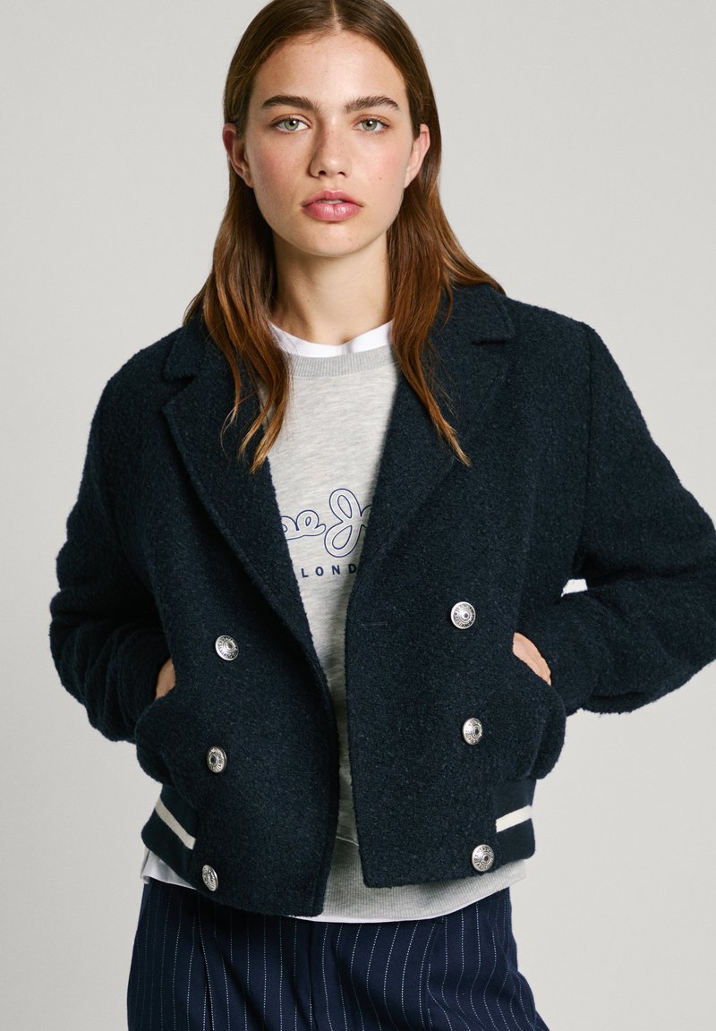 Marineblaue, doppelreihige Jacke aus Wollmischung mit großen silbernen Knöpfen, seitlichen Taschen und gestreiften Akzenten am Saum. Strukturierter Stoff.