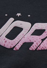 Sort stof med store, teksturerede bogstaver i pink og et spraglet mønster, ledsaget af små stjerneaccentuer over teksten.