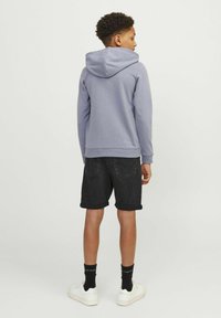 Sweatshirt à capuche gris, shorts en denim noir retroussés à l'ourlet, baskets blanches avec chaussettes noires. Design simple, coupe décontractée et texture douce.