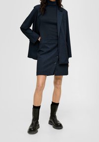 Marine gestreepte blazer met bijpassende rok met knoopaccenten, gecombineerd met een zwarte turtleneck en zwarte enkellaarzen. Gladde textuur.