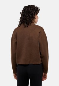 Pull court marron avec une texture côtelée, des épaules abaissées et une coupe décontractée. Il présente un col rond et des manches longues.