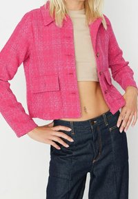 Fuchsia textuur gehaakte jas met een kraag, voor knopen en twee klepzakken, gecombineerd met donker denim broek.
