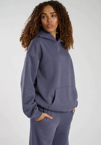 Överdimensionerad grå hoodie gjord av mjukt tyg, med en framficka, dragsko-huva och ribbade ärmslut, i kombination med matchande byxor.