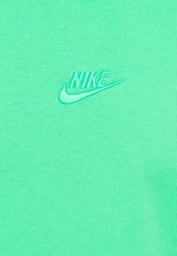 Tricou din bumbac verde deschis, cu un logo Nike brodat în aceeași culoare a firului, plasat pe partea stângă a pieptului.