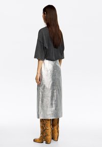 Oversized grijze top met korte mouwen, gecombineerd met een metallic zilveren rok. Schmaelchoenen hebben een bruin en zwart slangenprint met een hoge hak.