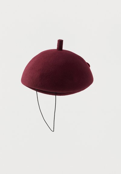 Bordowy filcowy kapelusz o zaokrąglonym, kopulastym kształcie z małym pionowym elementem na górze. Posiada czarną sznureczek do pewnego dopasowania. Gładka tekstura, minimalistyczny design.