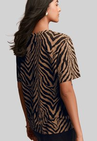 Tricou scurt cu mânecă, de culoare maro, având un model de dungi negre de tigru, dintr-un material moale, cu un croi lejer și decolteu rotunjit.