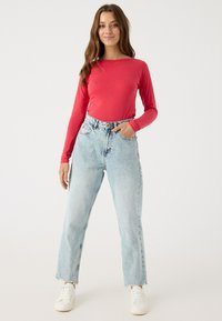 Top rojo de manga larga combinado con jeans de pierna recta azul claro de talle alto. El conjunto se completa con zapatillas blancas.