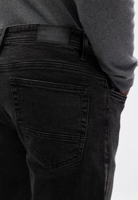 Czarne dżinsy z denimu o teksturowanym wykończeniu, z tylną kieszenią i metką INDICODE na pasku. Standardowy krój i design.