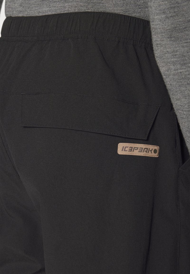 Czarne spodnie do wędrówek wykonane z lekkiego materiału, z elastycznym pasem, z tylną kieszenią oraz beżową metką z logo.