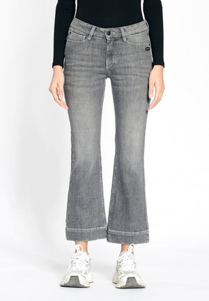 Gray flared jeans with a medium wash, featuring a mid-rise waist, subtle fading, and a stitched hem. Paired with white athletic sneakers.