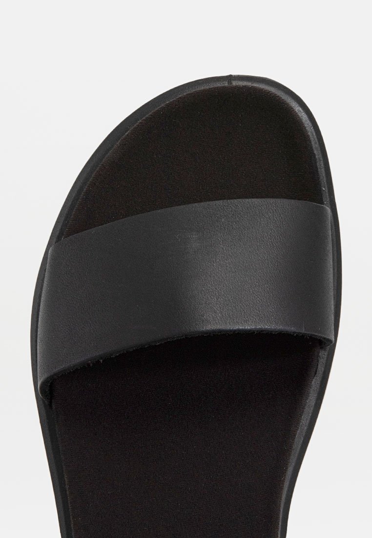 Schwarze Rutsch-Sandale mit einem breiten matten Riemen, flacher Sohle und glatter Innenoberfläche. Entwickelt für einfaches Hineinschlüpfen.