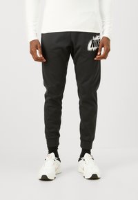 Mustat urheiluhousut, joissa on tekstuuri, tiukat resorit ja suuri valkoinen Nike-logo vasemmassa reidessä. Suunniteltu mukavuutta varten.