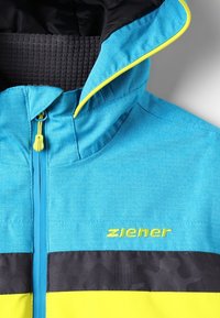 Blå jacka med svarta och gula detaljer, har en texturerad huva, full dragkedja och "ziener"-logotyp i livlig gul över bröstet.