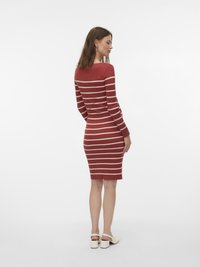 Piros bordázott ruha fehér vízszintes csíkokkal, testhez simuló fazon, hosszú ujjú, térdig érő. A modell fehér sarkú szandált visel.