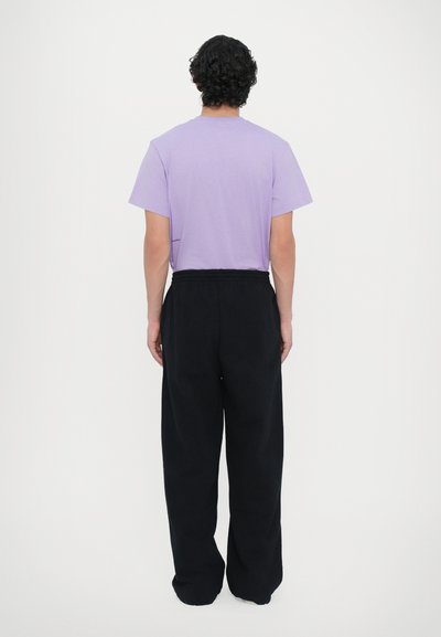 T-shirt en coton violet à manches courtes, associée à un pantalon de survêtement noir ample. Design minimaliste avec une taille élastique.
