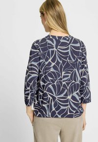 Marineblauwe blouse met een bladerenpatroon in lichtblauw en room. Heeft driekwartmouwen en een comfortabele pasvorm, gemaakt van een zachte stof.
