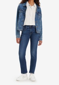 Chaqueta de denim azul con un corte relajado, combinada con una camisa blanca a rayas, jeans oscuros y zapatillas blancas. Diseño sencillo, colores clásicos.