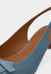 Chaussure plate à lanière arrière en cuir bleu clair avec un bout pointu et un nœud décoratif cousu à l'avant.