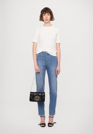 Maglietta bianca a maniche corte, jeans blu a gamba dritta, borsa nera trapuntata con hardware dorato e sandali neri con fiocchi.