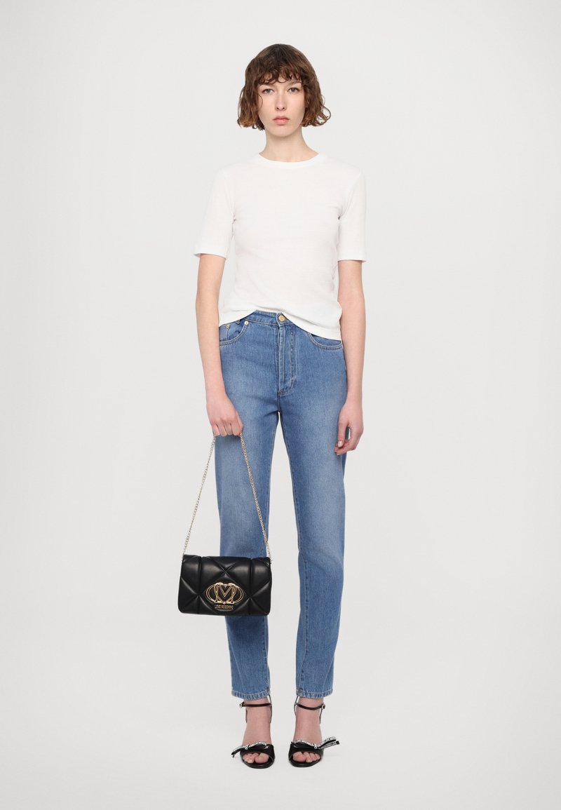 Maglietta bianca a maniche corte, jeans blu a gamba dritta, borsa nera trapuntata con hardware dorato e sandali neri con fiocchi.
