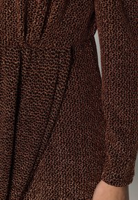Robe en bronze scintillante avec un motif léopard, des manches longues et une taille cintrée. Fabriquée en tissu texturé et doux.