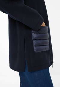 Cappotto in lana blu navy con cerniera laterale, caratterizzato da una tasca gonfia in nylon di texture blu scuro a contrasto e un design a vestibilità comoda.