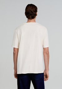Camiseta de algodón de manga corta y cuello redondo en color blanco roto, con un diseño minimalista y un ajuste holgado, con la parte trasera lisa.