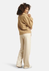 Tan textured fleece jacket with a shawl collar, paired with cream wide-leg trousers. The outfit features a relaxed fit and soft materials.
