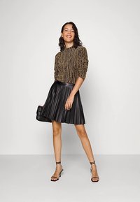 Falda negra plisada con una cintura lisa, combinada con un top de manga larga de textura dorada con costillas verticales. Tacones negros sencillos.